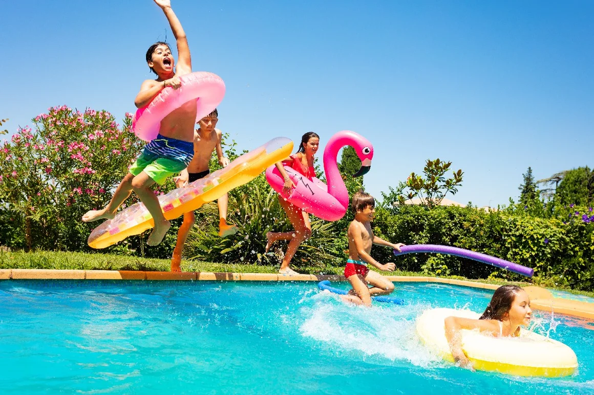 Fünf Kinder springen mit Schwimmreifen in einen Pool.